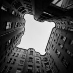 Upward view of dark buildings framing a bright sky.