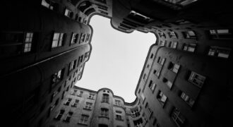 Upward view of dark buildings framing a bright sky.